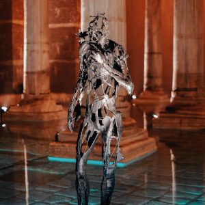 Contemporary metal sculpture showcased in a dimly lit gallery with architectural columns.