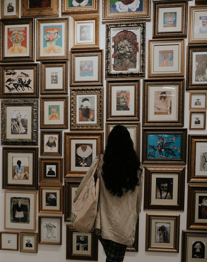 A woman observes a diverse collection of framed artwork in a museum gallery.